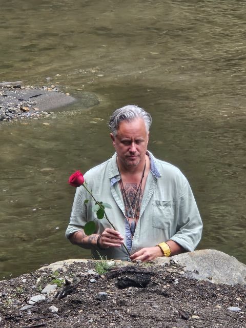 man in a lake holding a rose near a boulder